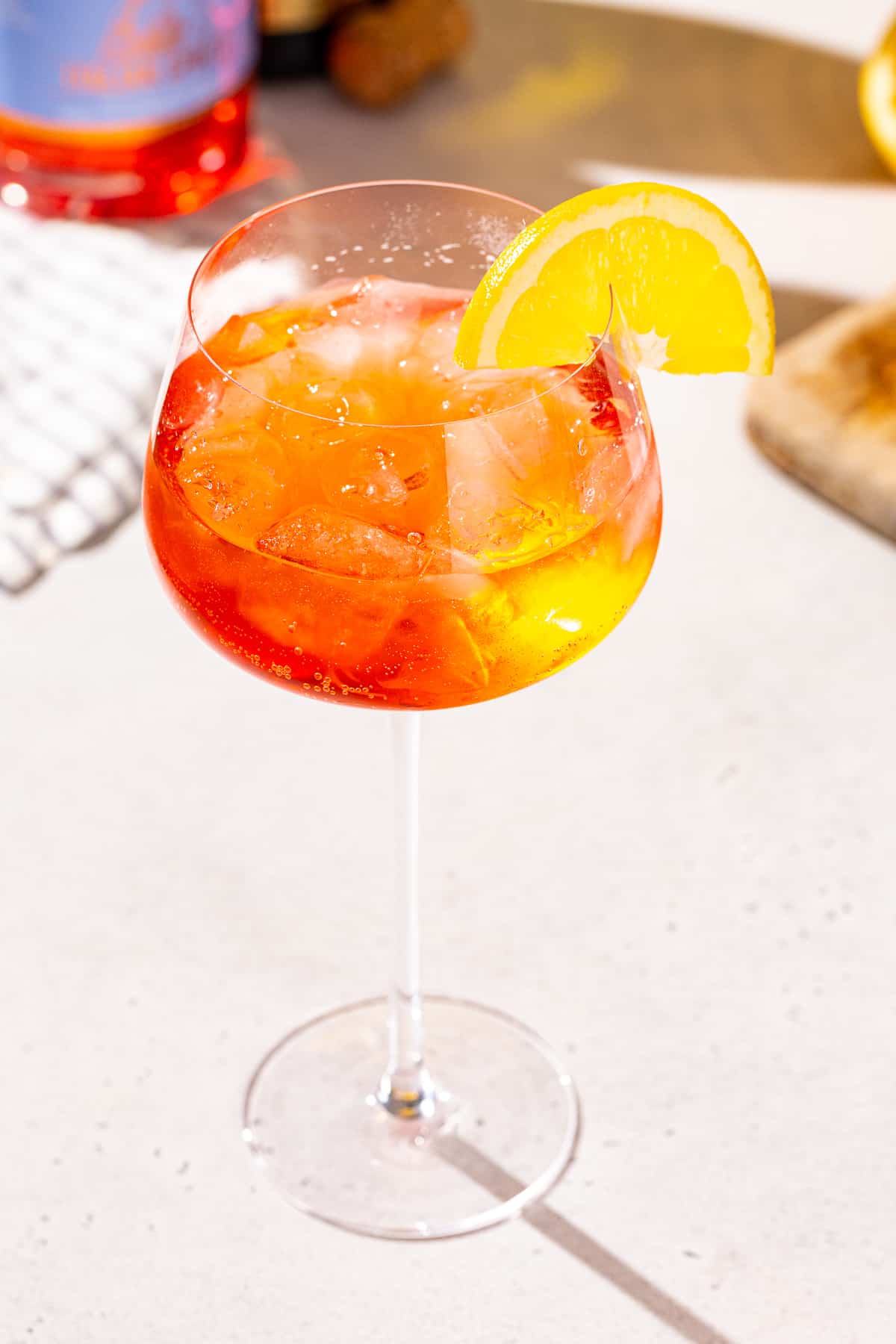 Slightly overhead view of an Aperol Spritz mocktail on a countertop. Some ingredients can be seen in the background.