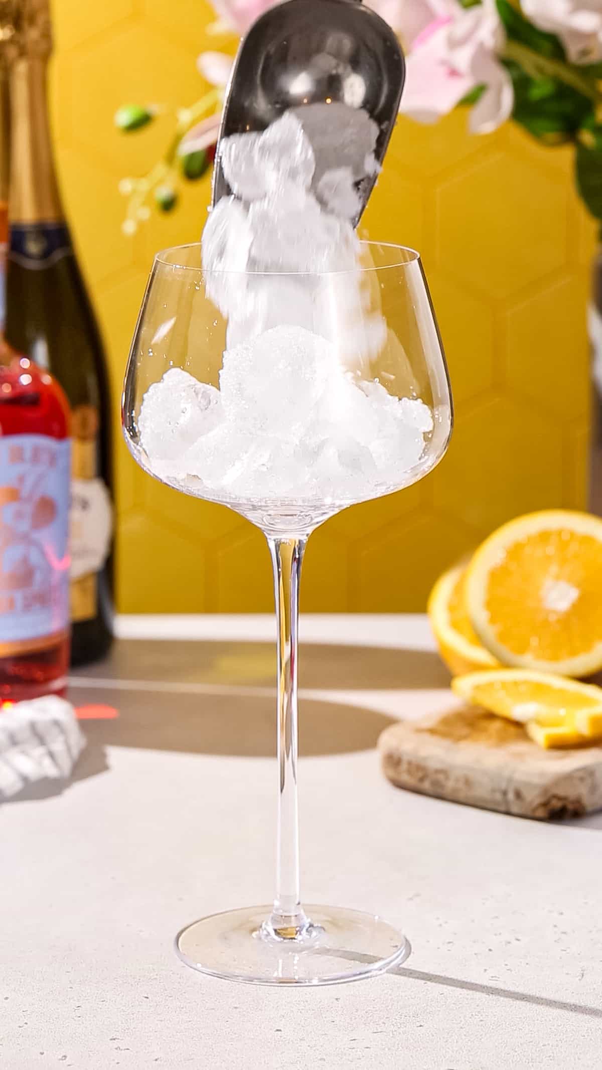 Hand using an ice scoop to add ice to a large spritz glass.