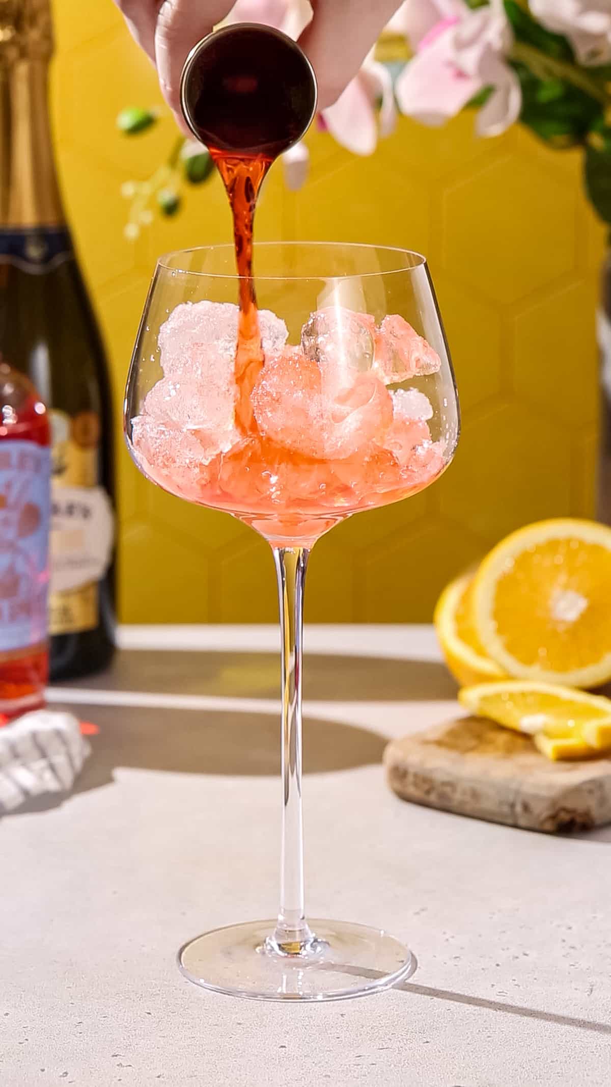 Hand pouring non-alcoholic aperitif into a spritz glass filled with ice.