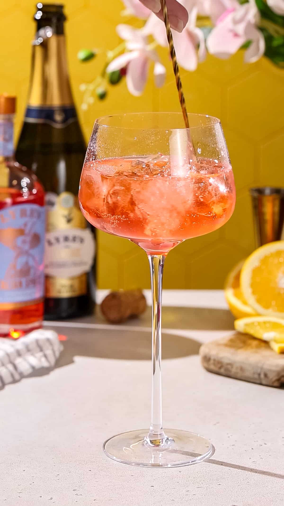 Hand using a long bar spoon to gently stir a spritz cocktail.