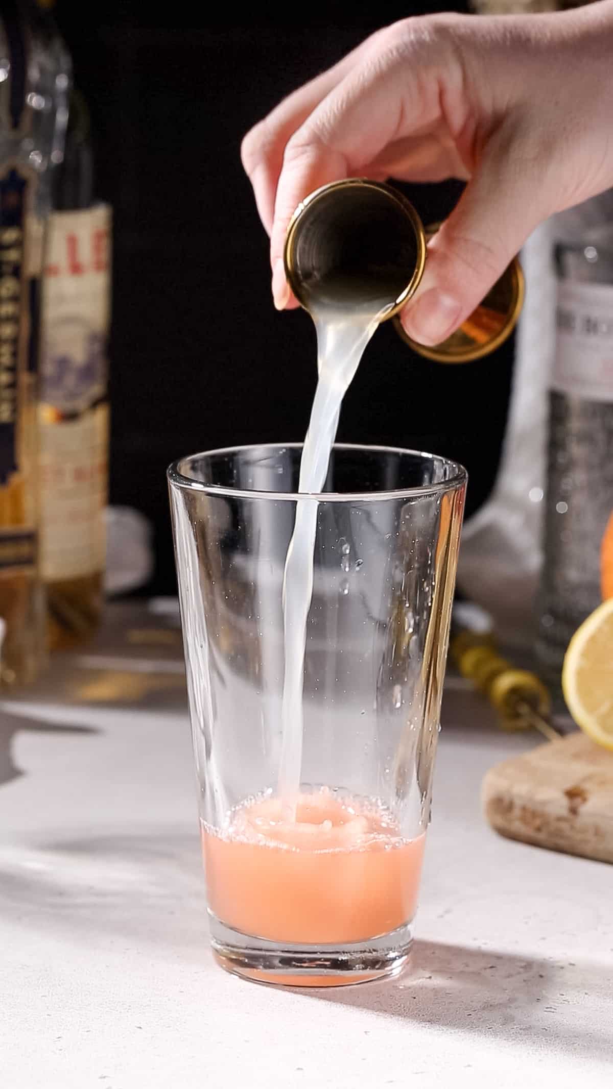 Hand pouring lemon juice into a cocktail shaker.