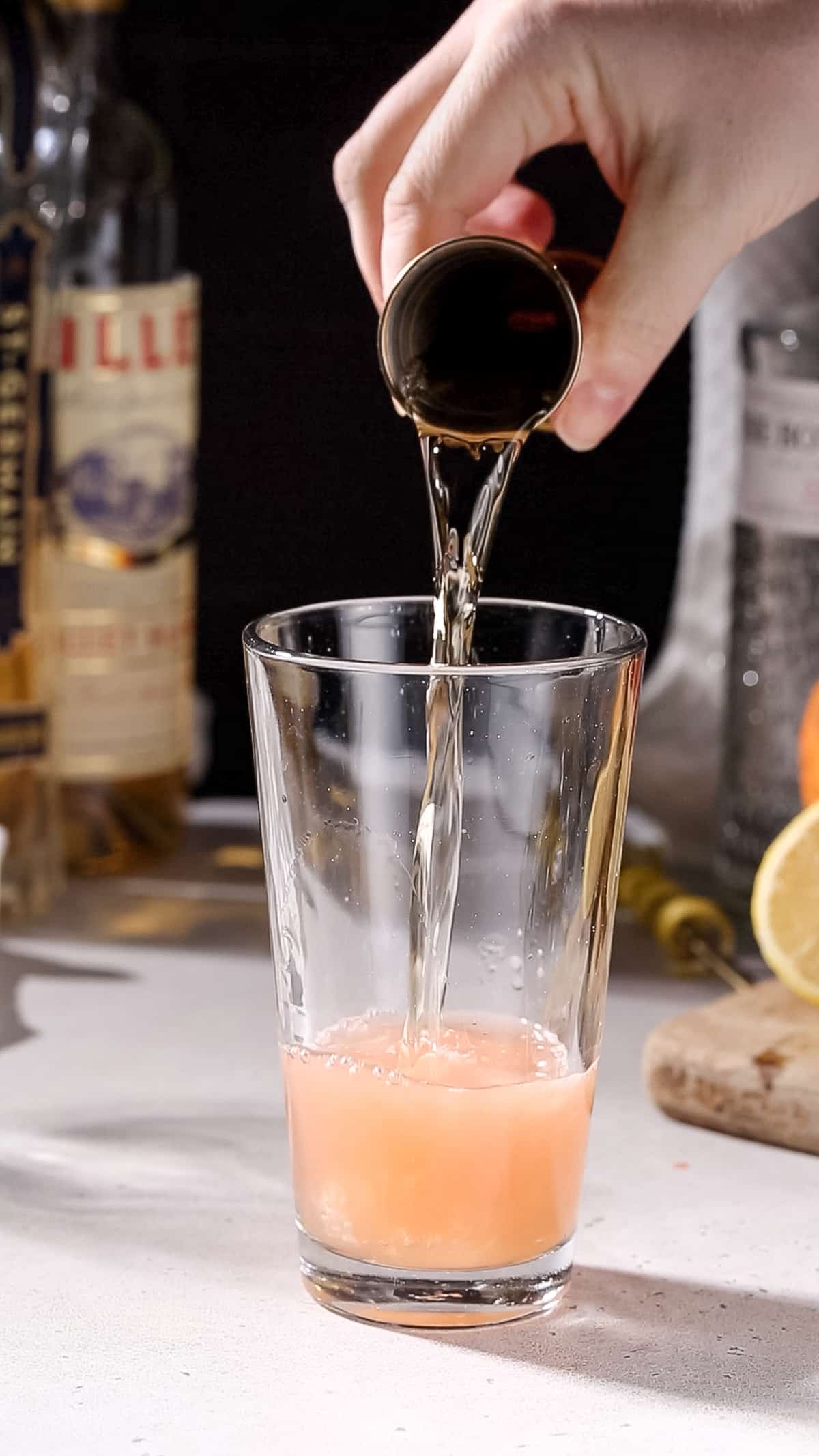 Hand pouring lillet blanc into a cocktail shaker.
