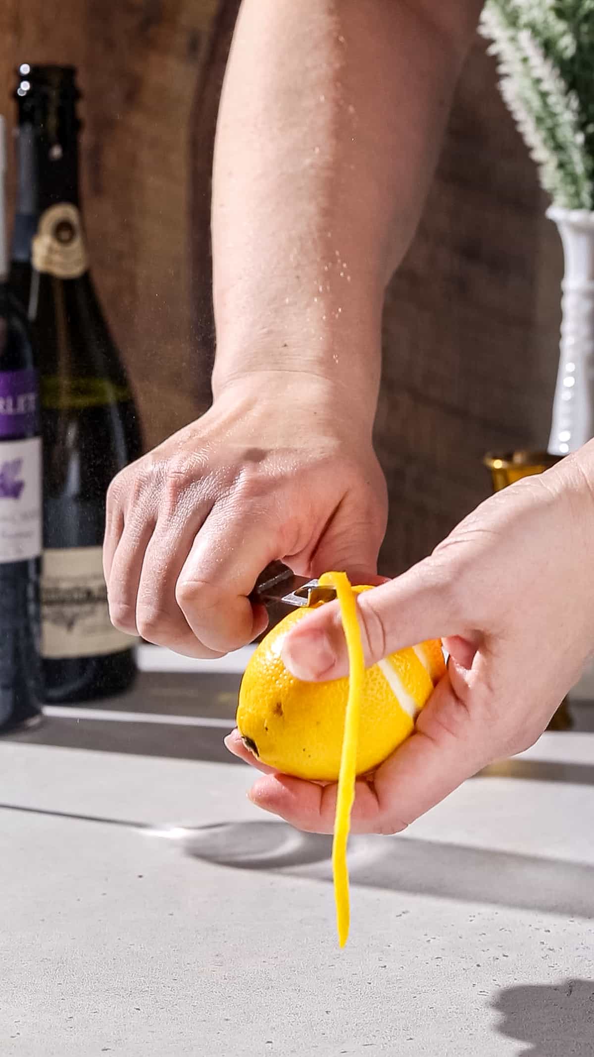 Hands using a channel knife to peel a long strip of lemon peel.