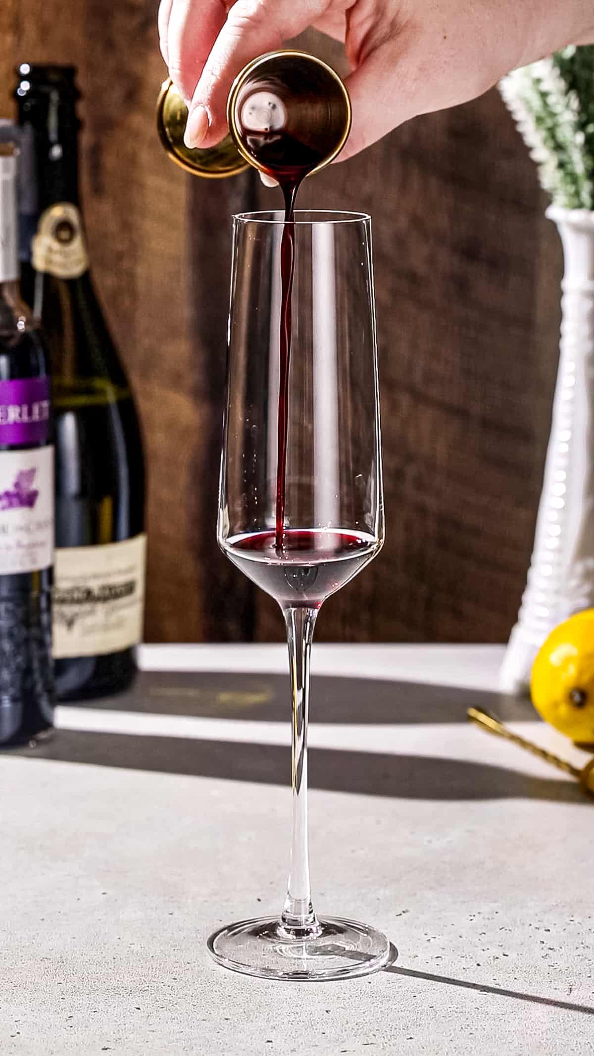 Hand pouring creme de cassis liqueur into a champagne flute.