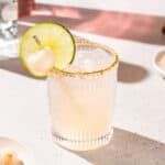 Lychee Margarita garnished with a lime and a lychee fruit on a countertop.