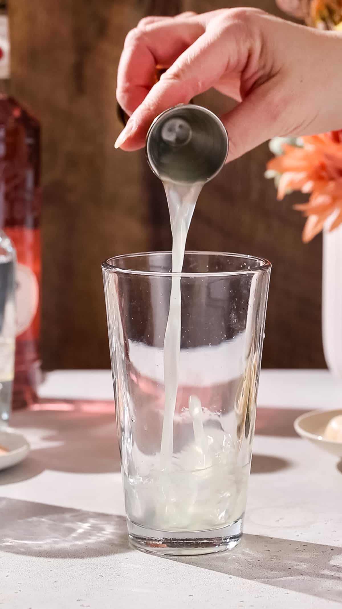 Hand pouring lime juice into a cocktail shaker.