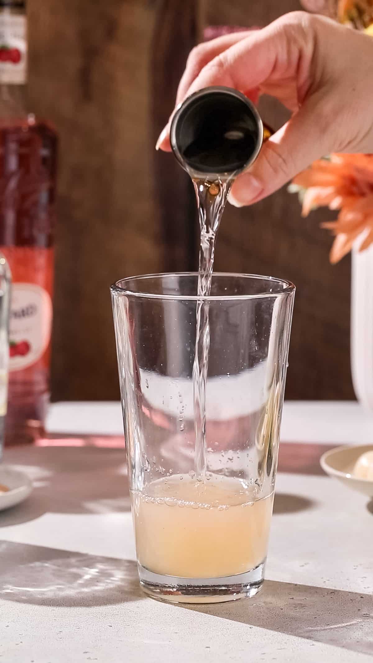 Hand pouring tequila into a cocktail shaker.