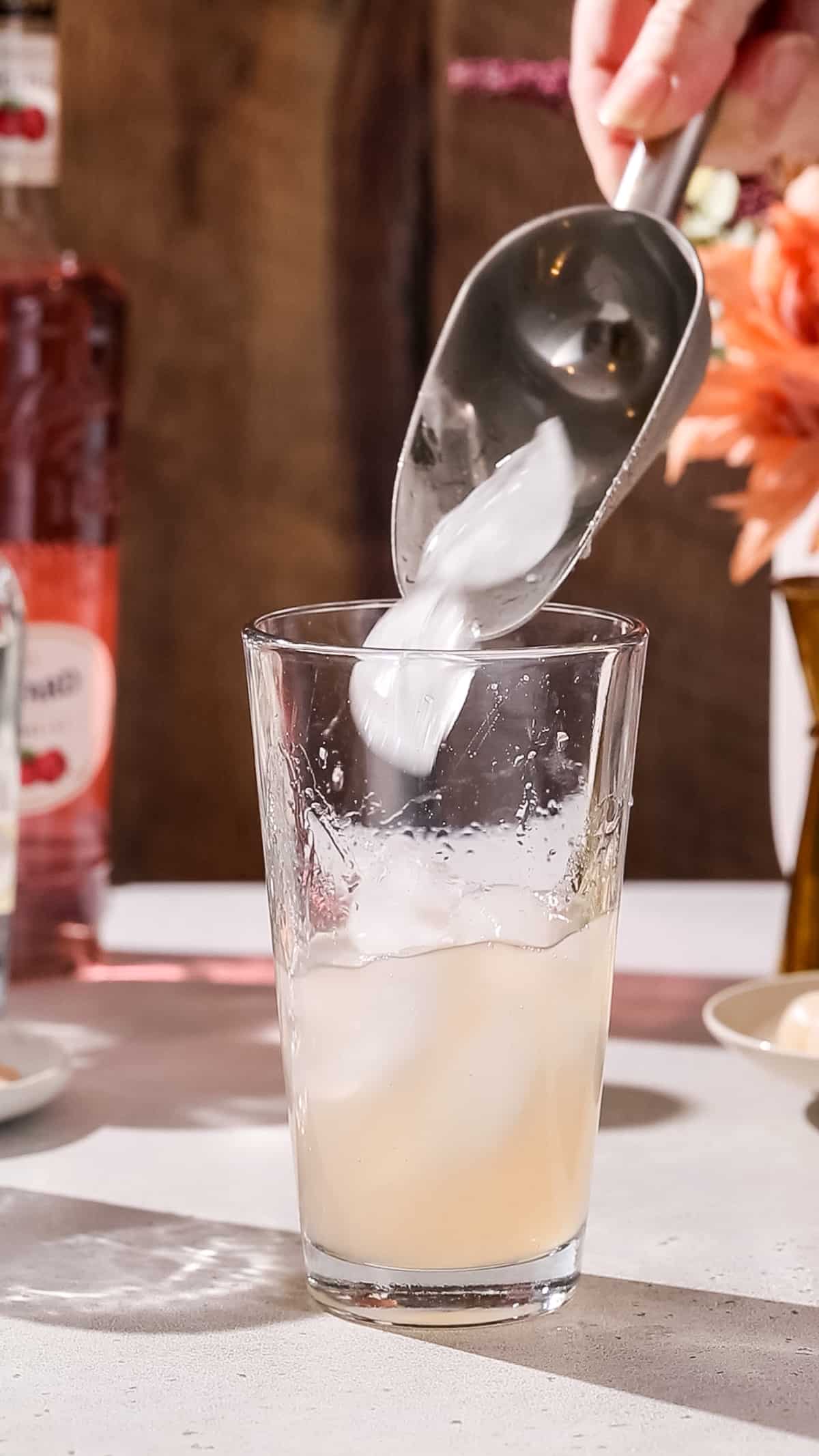 Hand adding ice to a cocktail shaker.