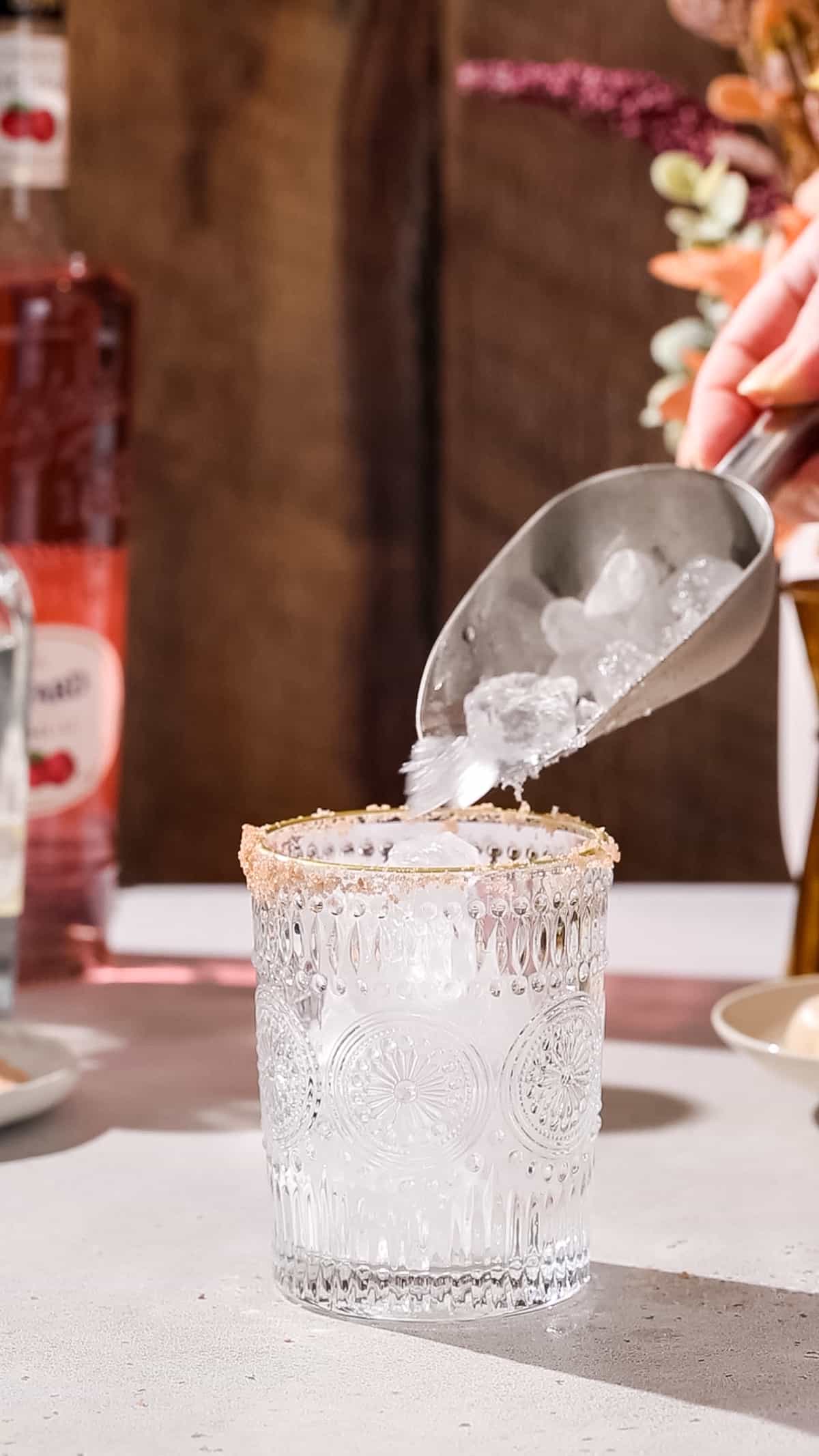 Hand adding ice to a salt-rimmed cocktail glass.