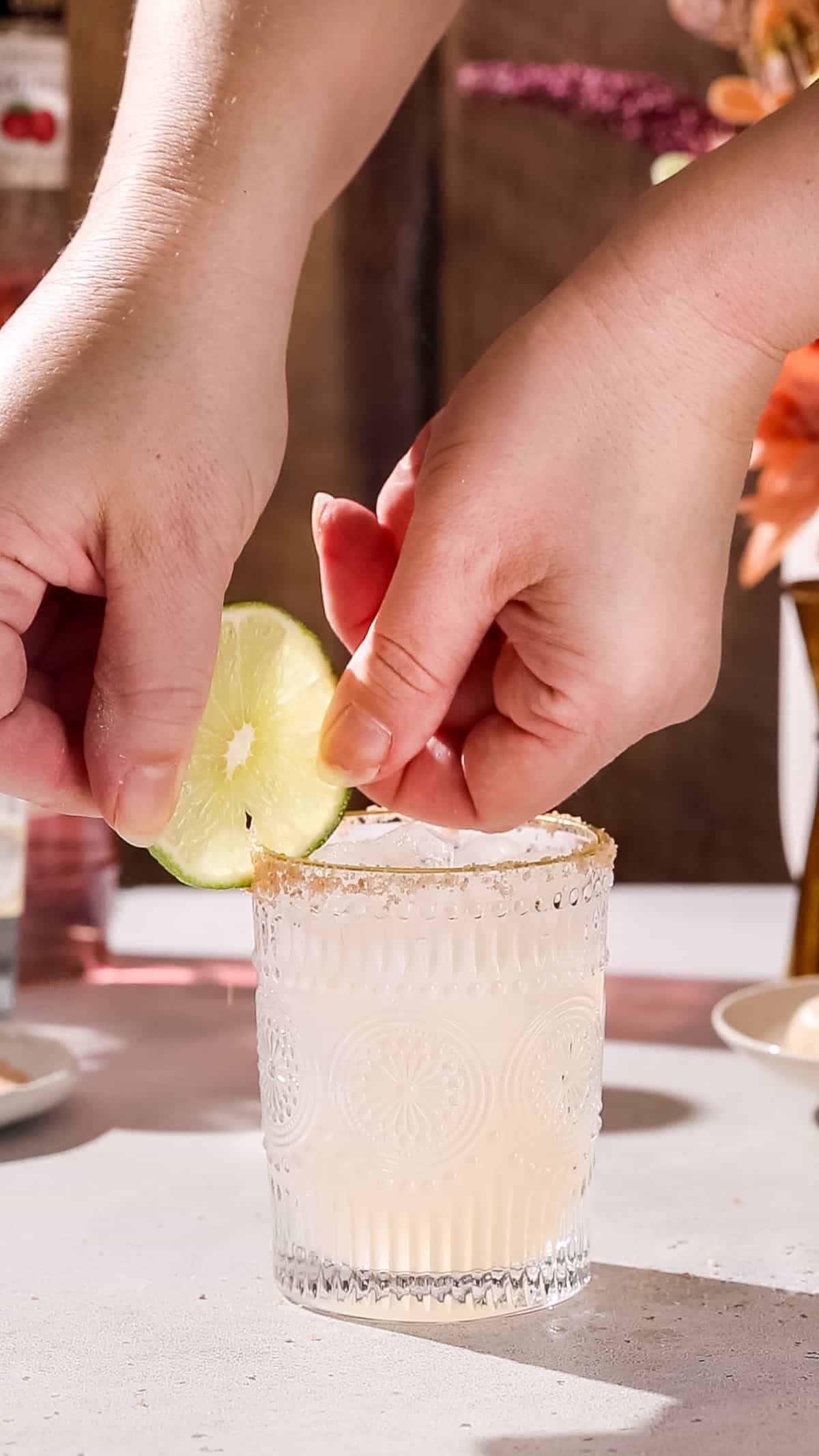 Hands adding a slice of lime to the rim of a glass.