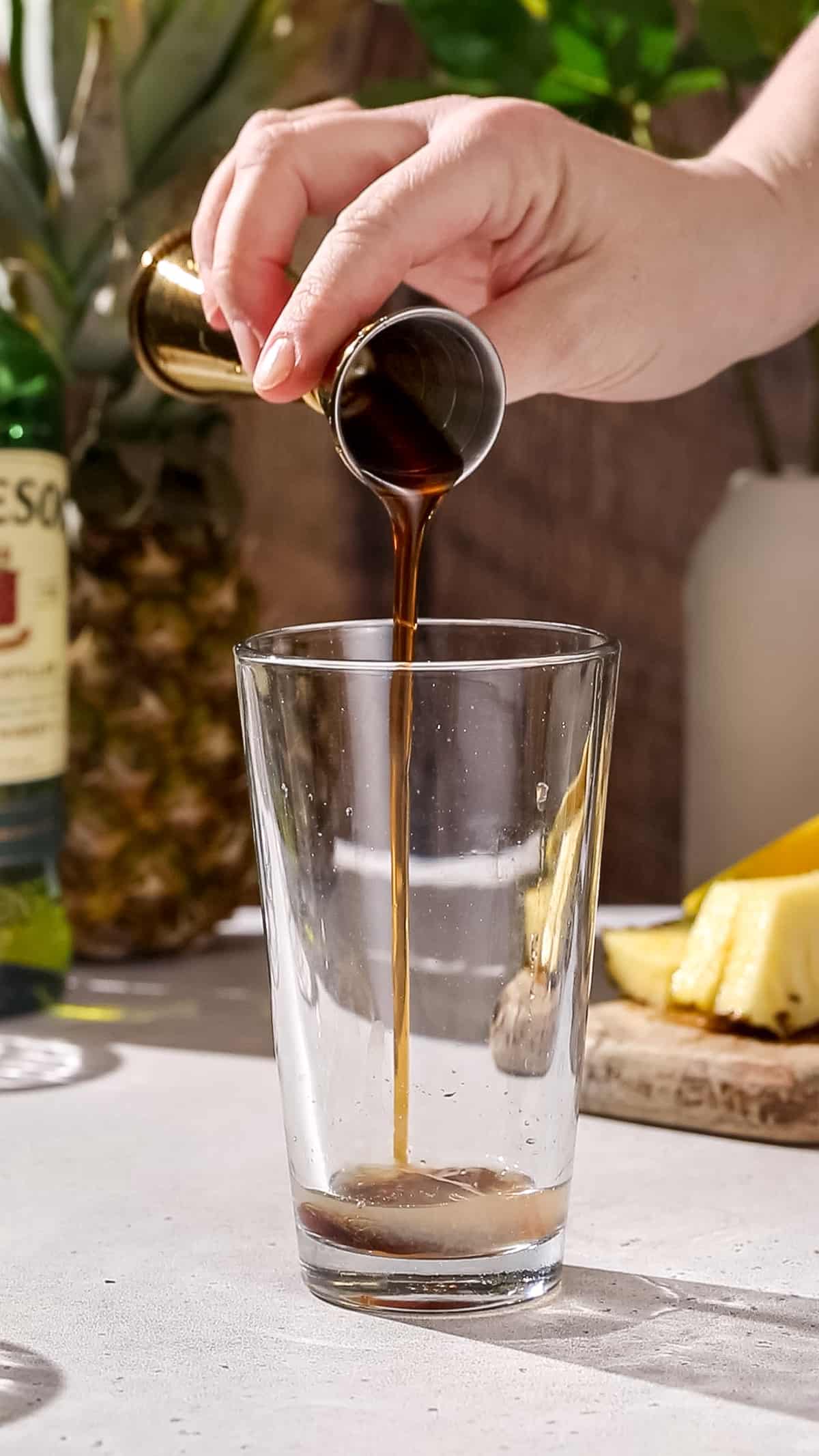 Hand pouring maple syrup into a cocktail shaker.