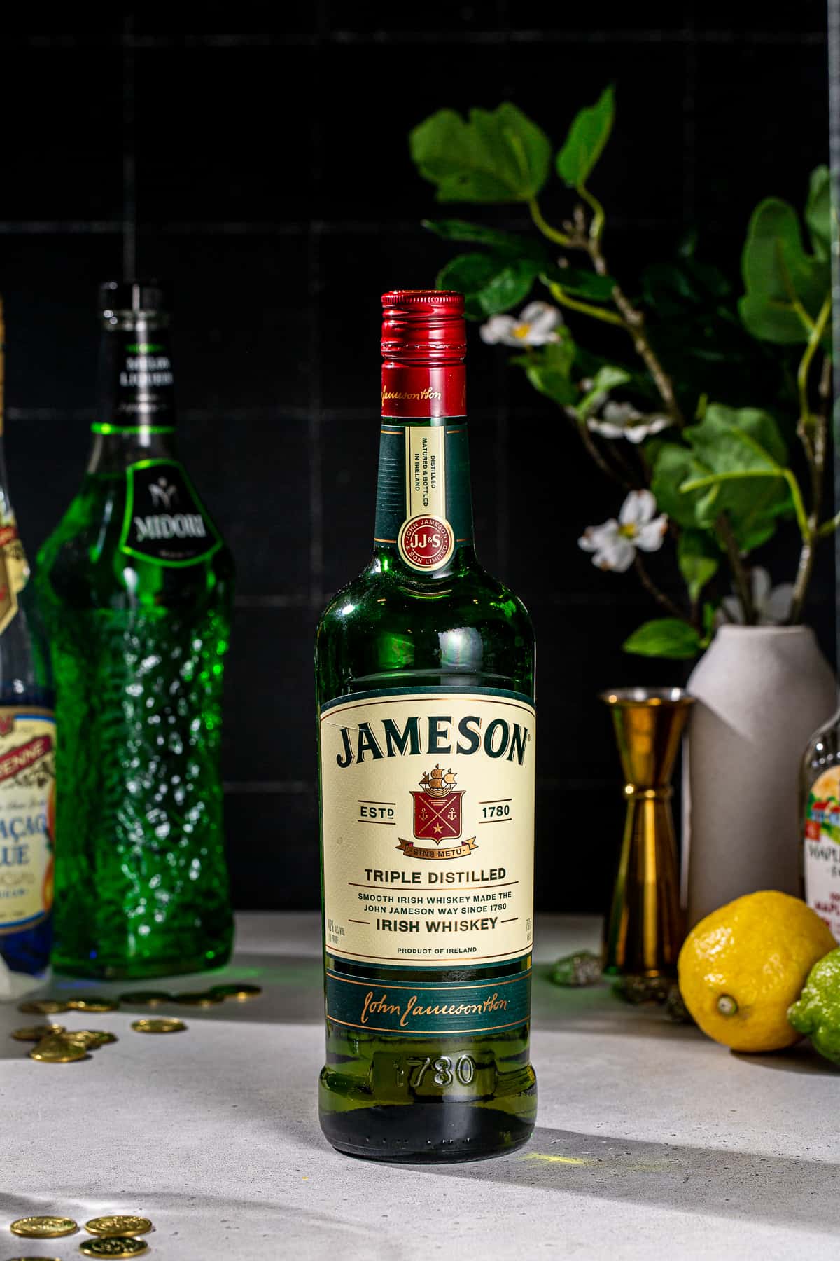 A bottle of Jameson Irish Whiskey with some other bottles and cocktail accessories in the background.