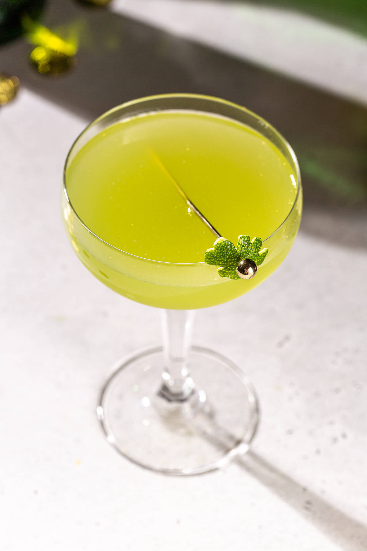 Overhead view of a green Shamrock Sour cocktail. The drink is garnished with a lime peel in the shape of a shamrock held by a cocktail pick.