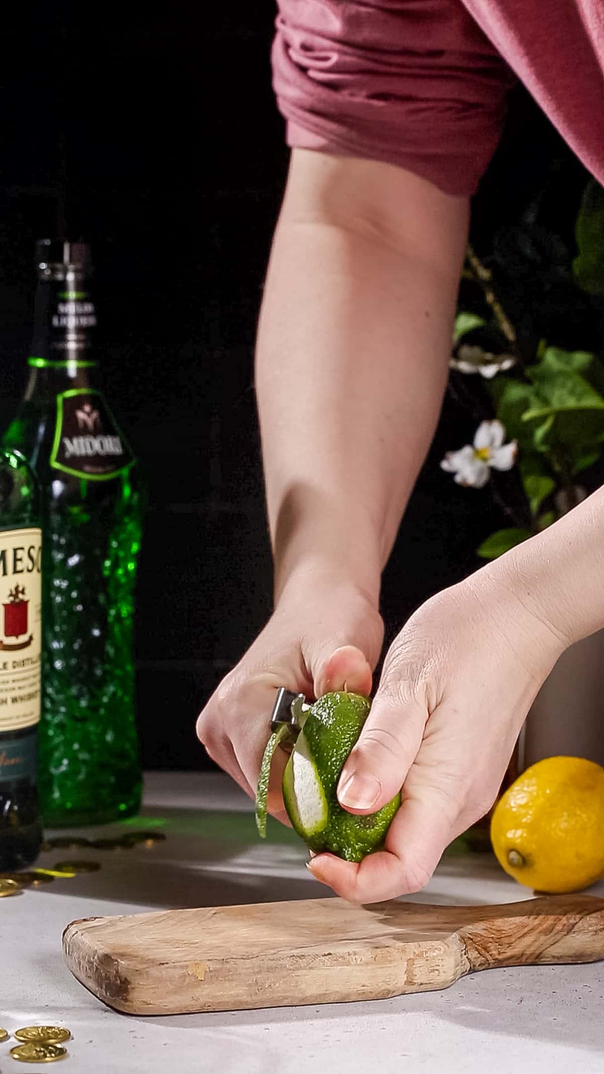 Hands using a vegetable peeler to cut a piece of lime peel.