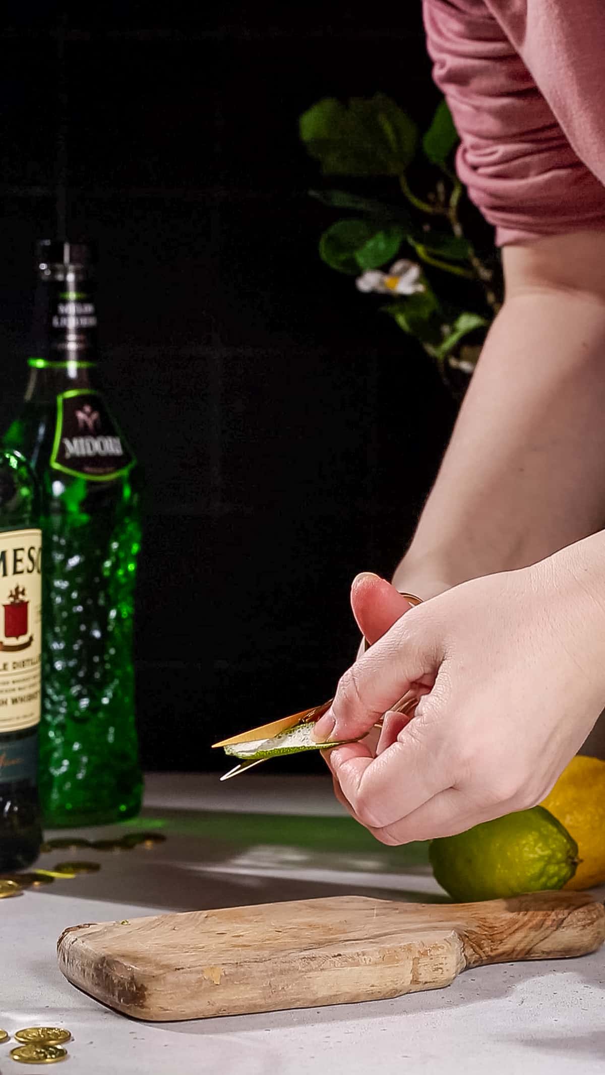 Hands using food scissors to cut the lime peel into the shape of a shamrock.