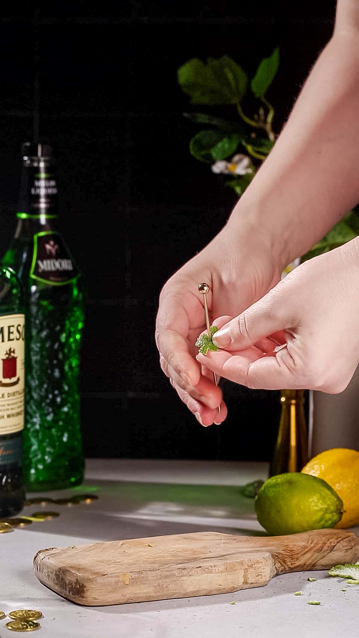 Hand using a cocktail pick to skewer a lime peel in the shape of a shamrock to add to a cocktail as a garnish.