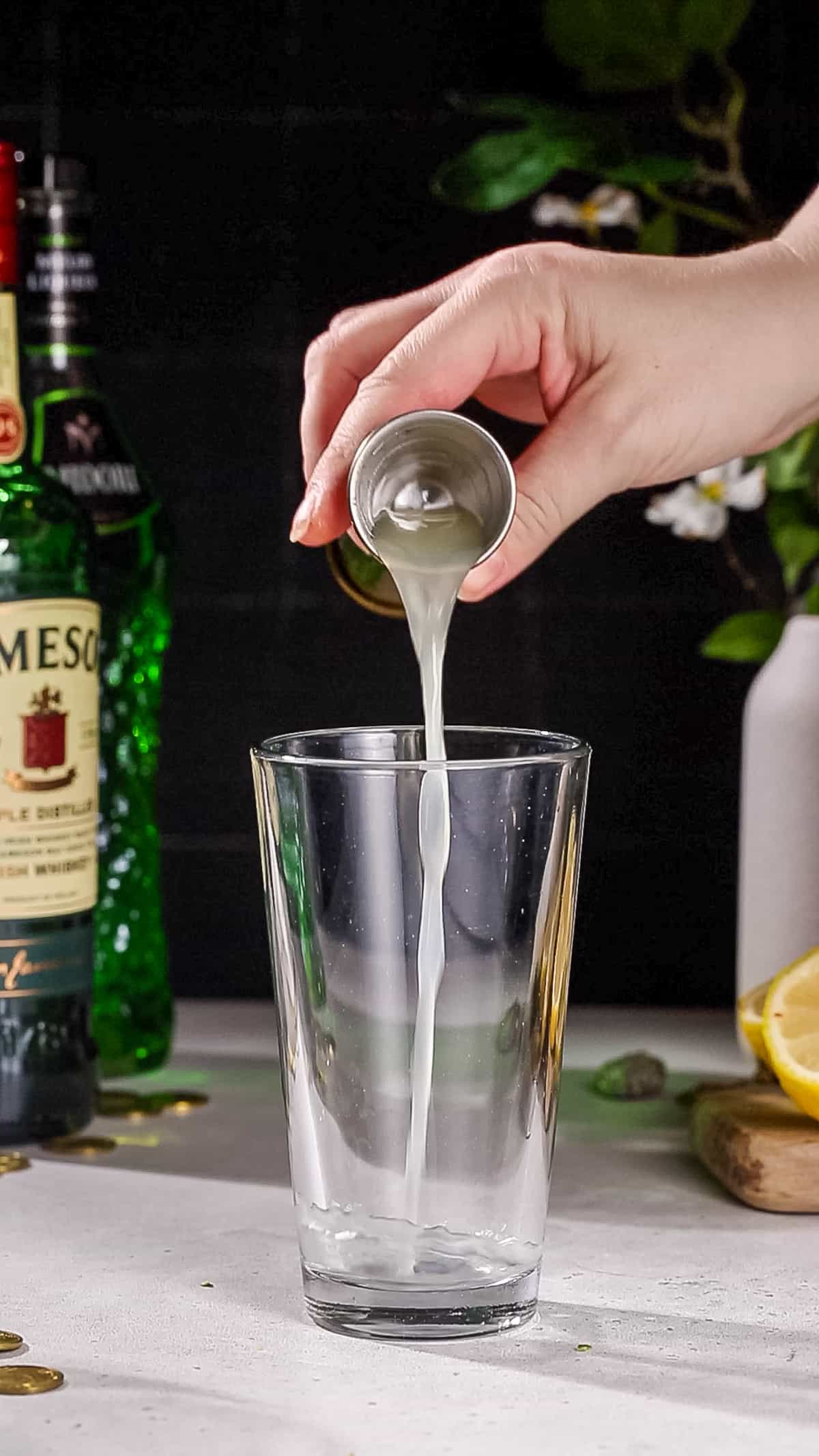 Hand adding lime juice to a cocktail shaker.