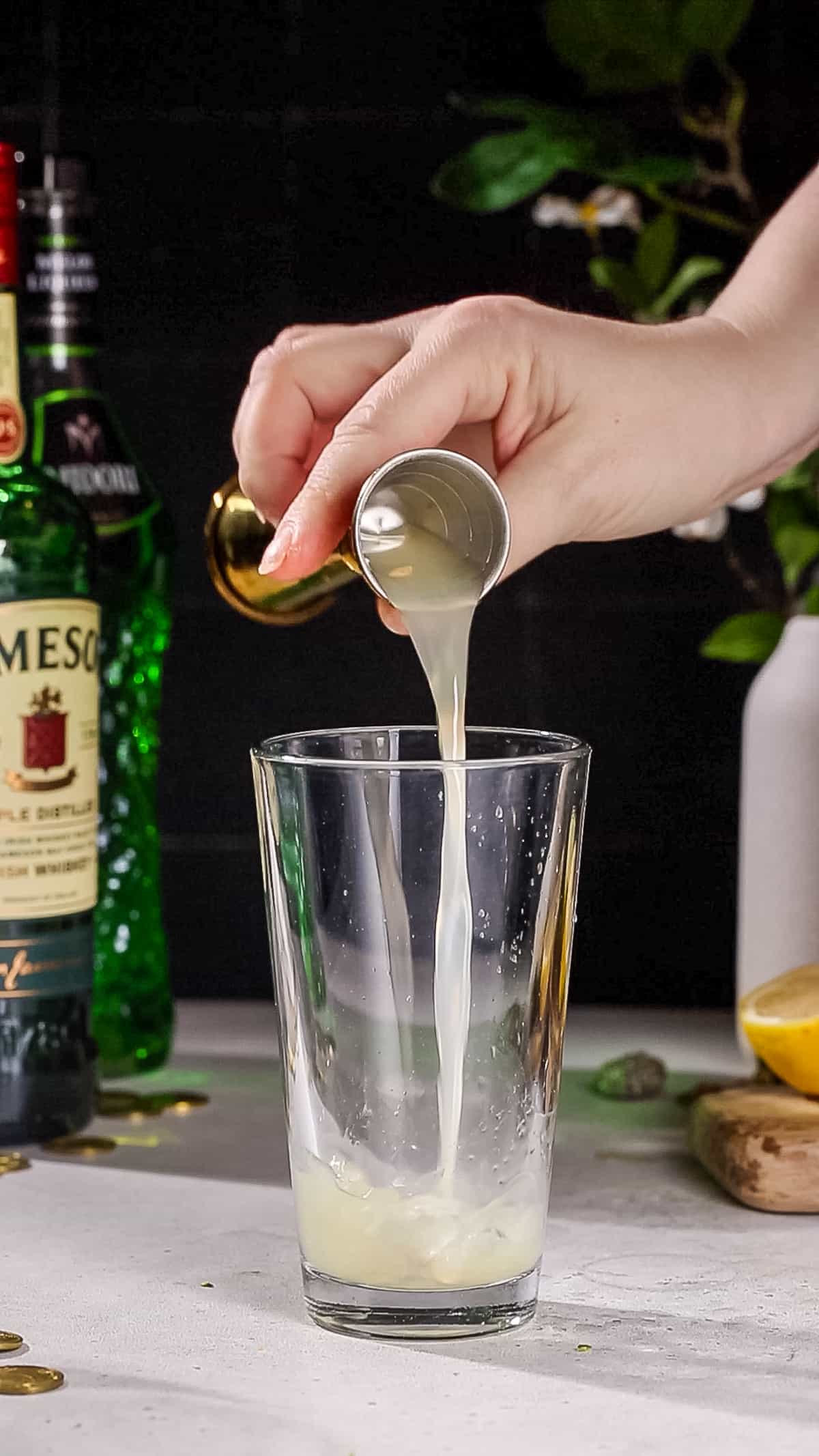 Hand adding lemon juice to a cocktail shaker.