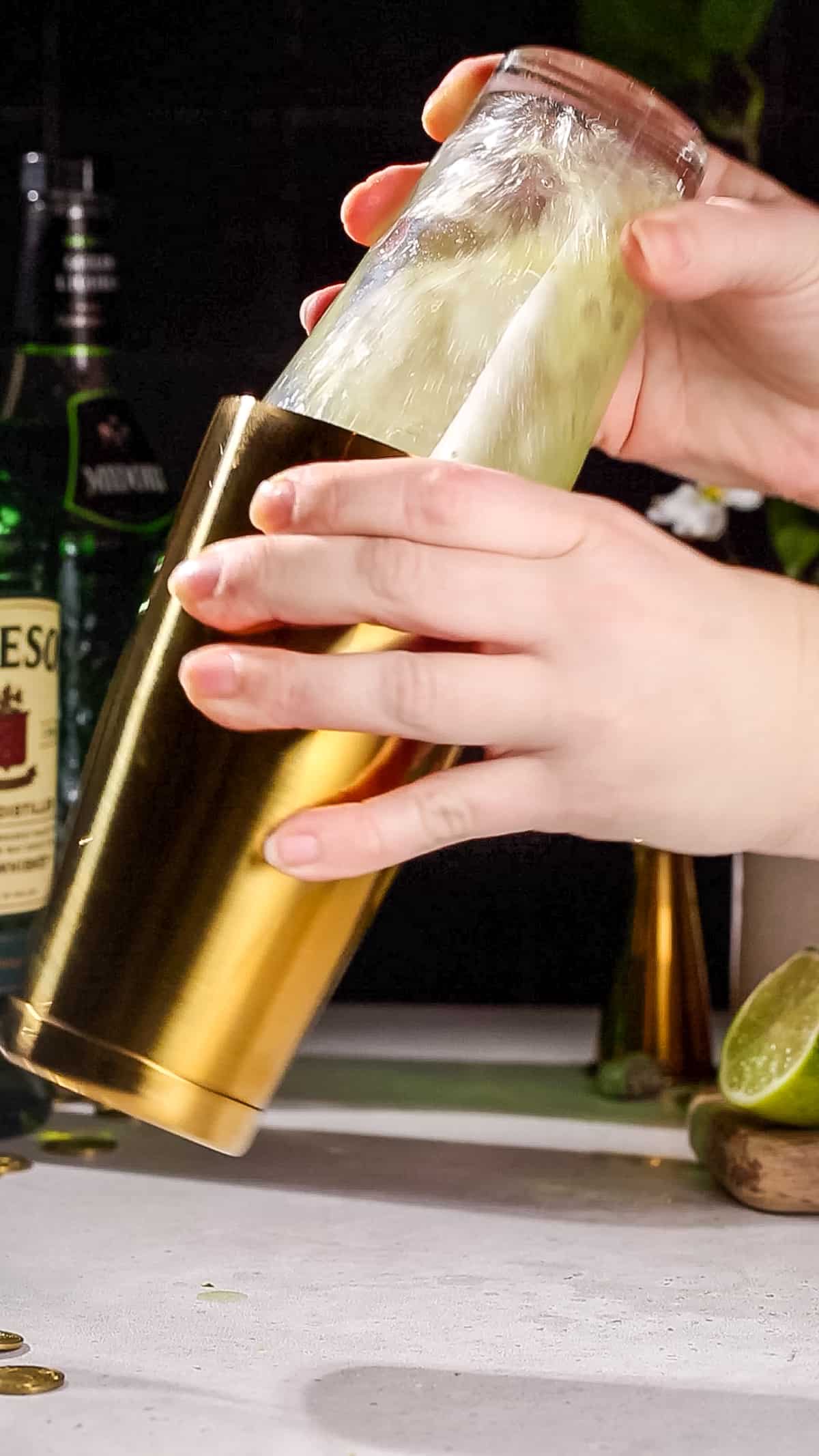 Hands shaking up a cocktail using a gold and glass cocktail shaker.