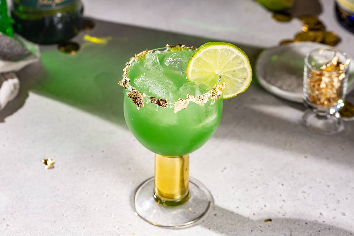 Overhead view of a green colored Irish Margarita cocktail with a lime and edible gold garnish.