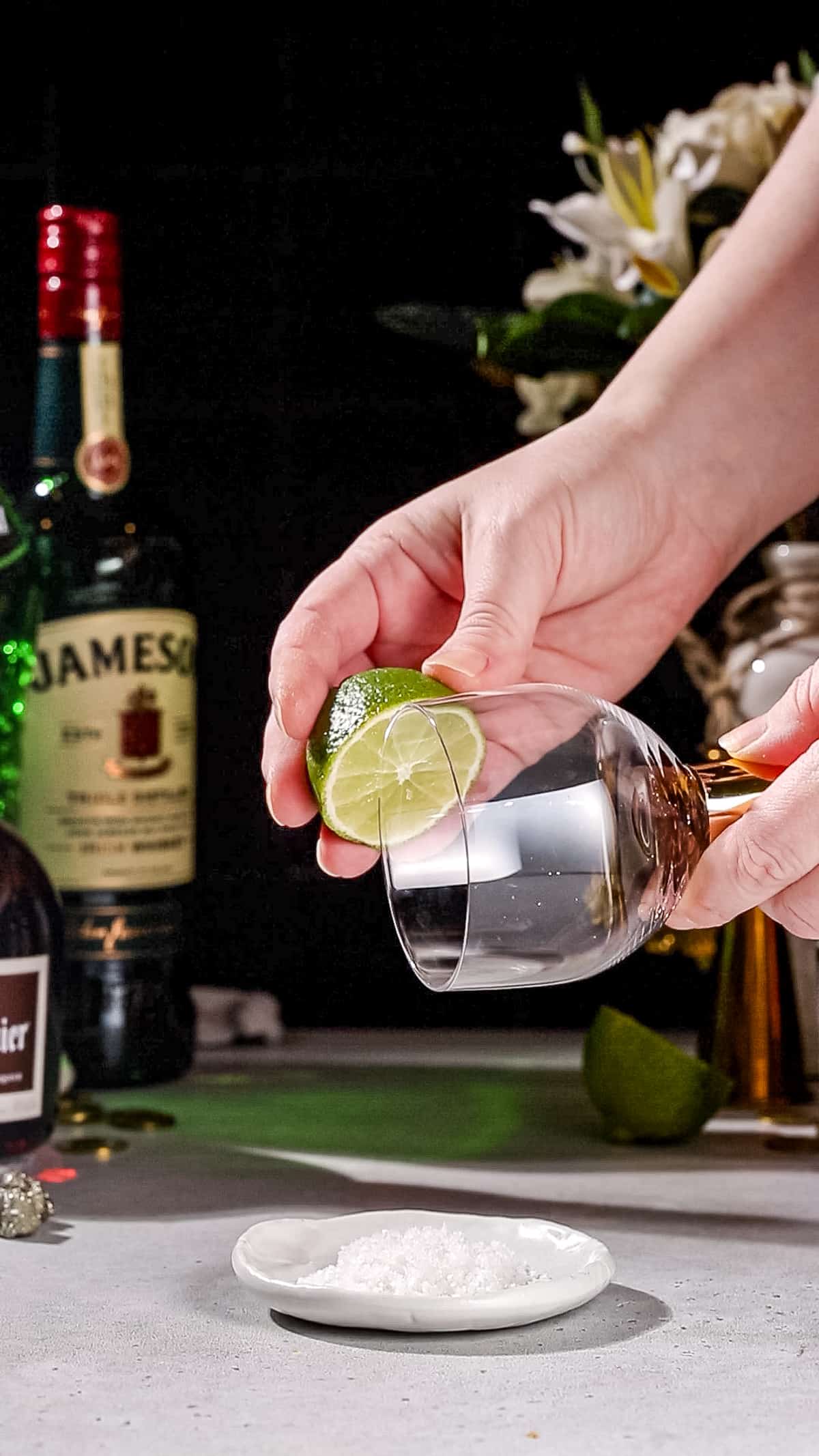 Hand using a cut lime to wet the rim of a cocktail glass.