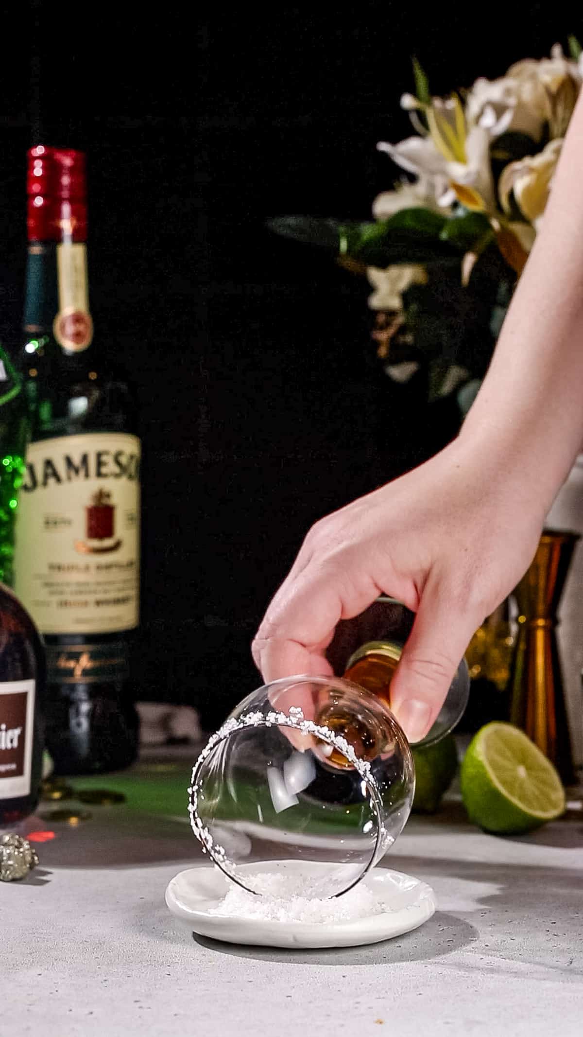 Hand dipping the rim of a cocktail glass into a dish of salt.