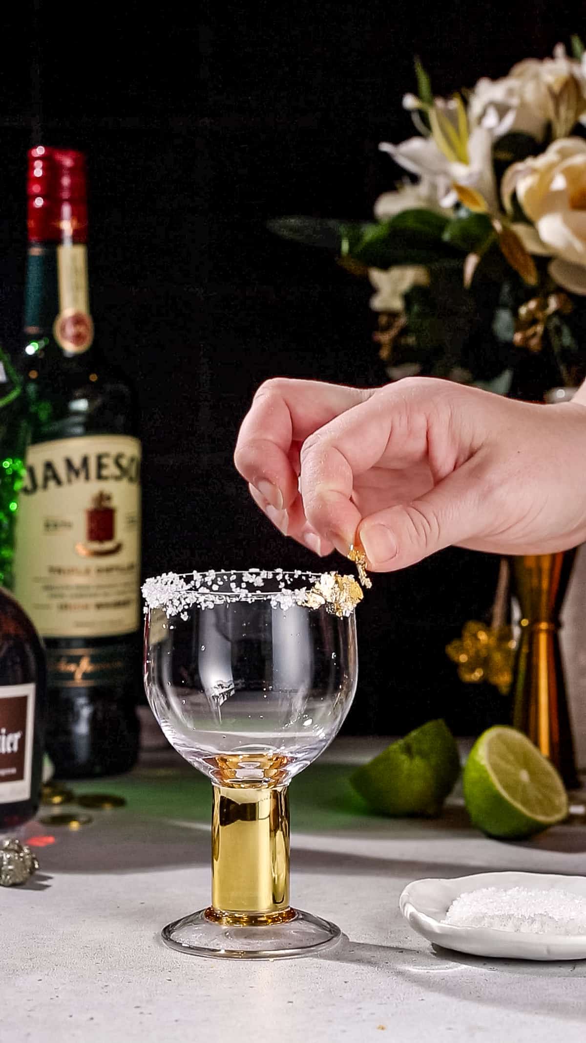 Hand adding pieces of edible gold leaf to the rim of a cocktail glass.