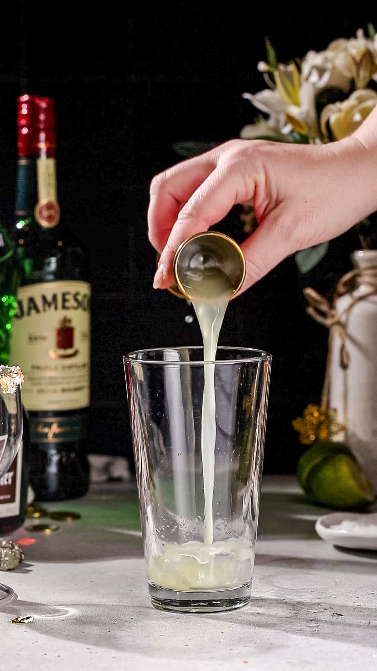 Hand adding lime juice to a cocktail shaker.