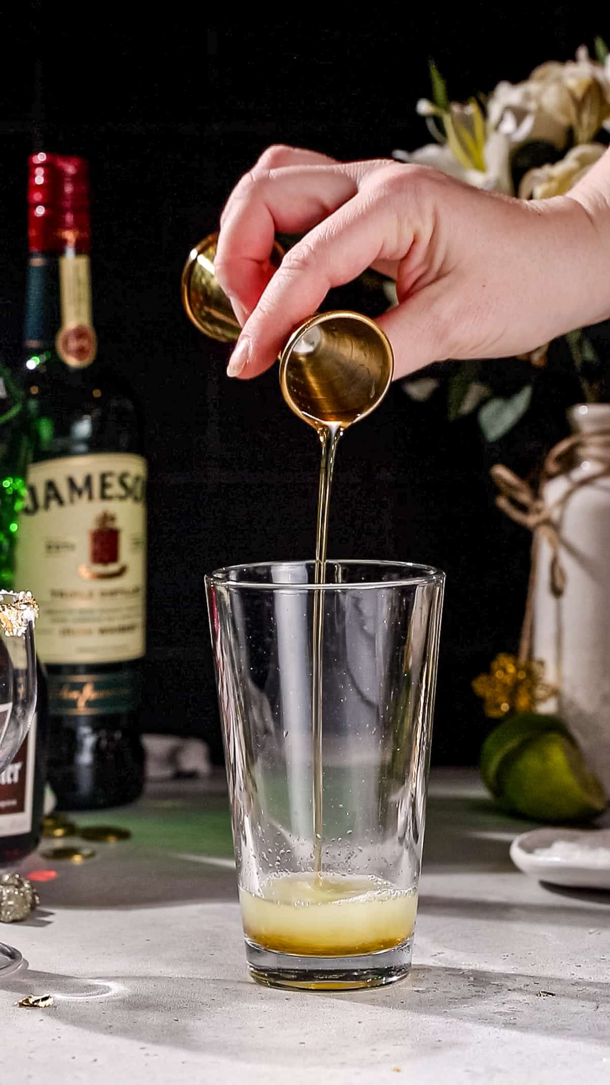 Hand adding maple syrup to a cocktail shaker.