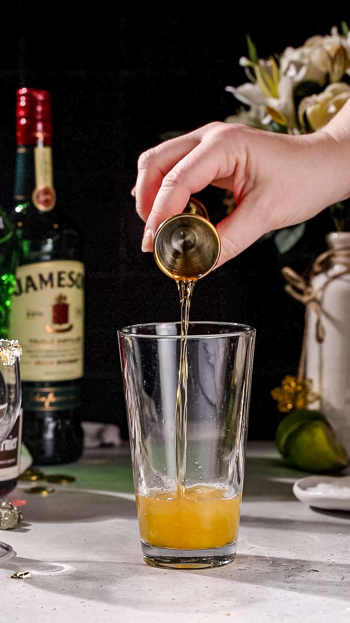 Hand adding grand marnier liqueur to a cocktail shaker.