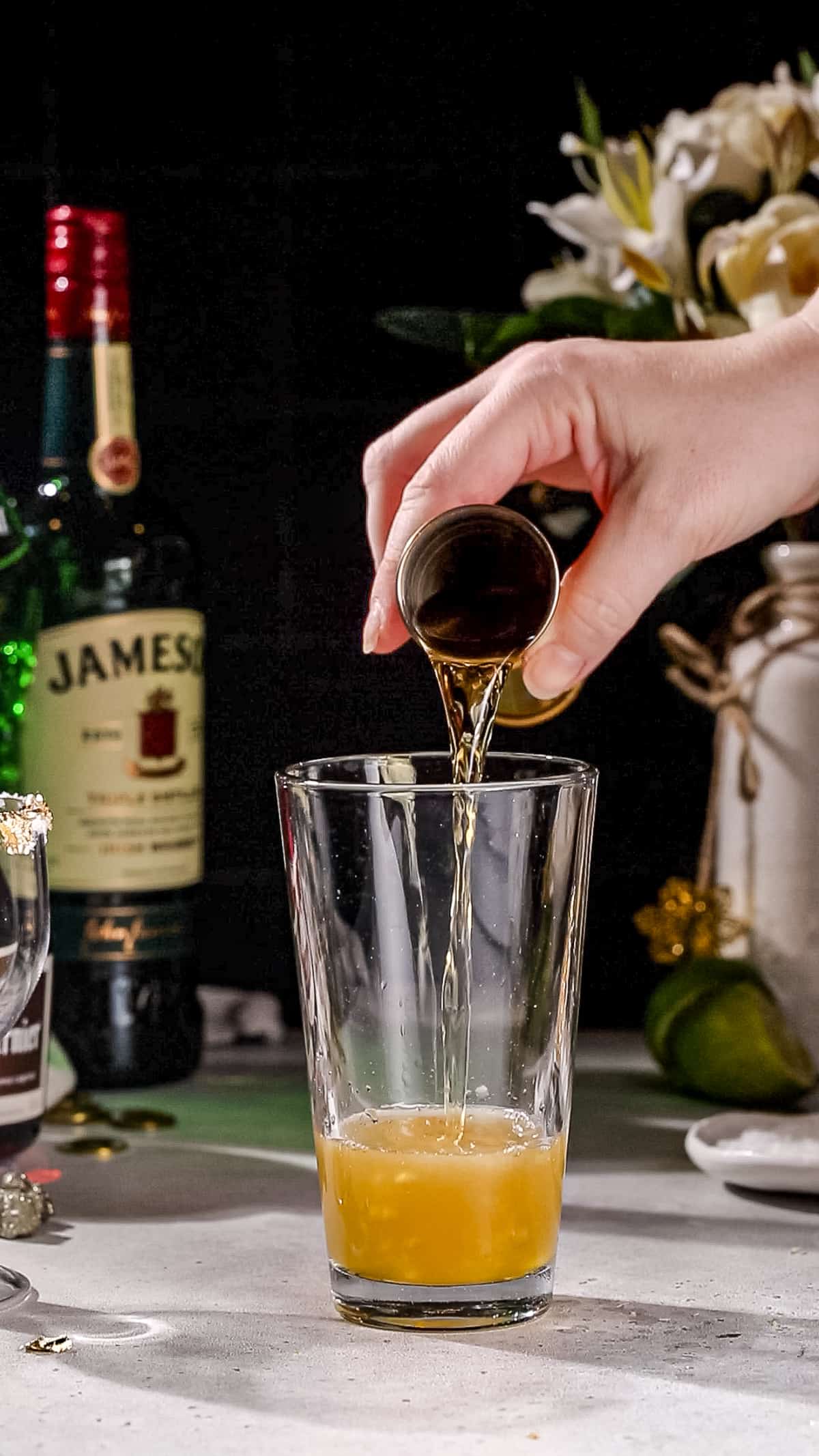 Hand adding Irish whiskey to a cocktail shaker.