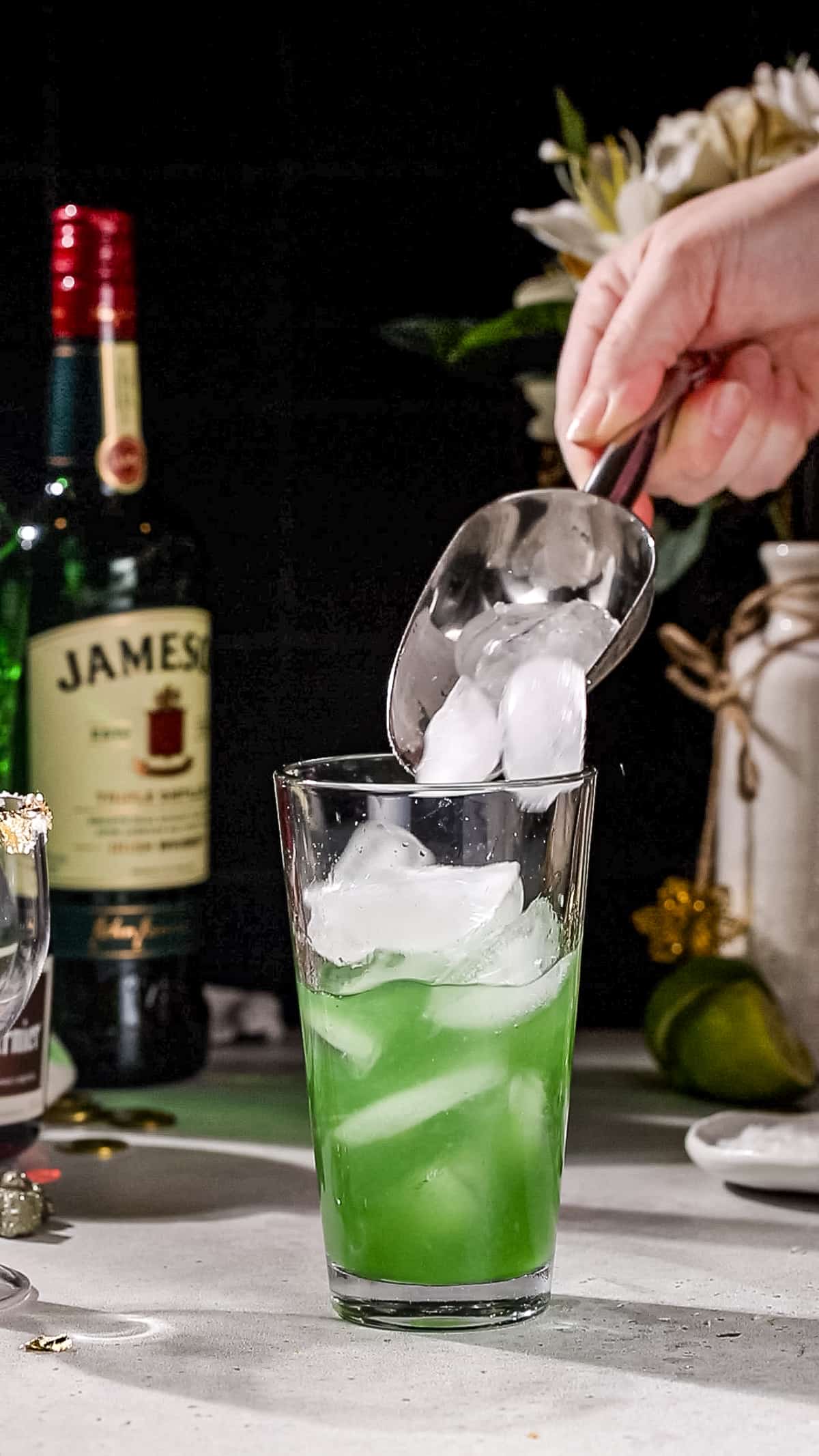 Hand using an ice scoop to add ice cubes to a cocktail shaker.