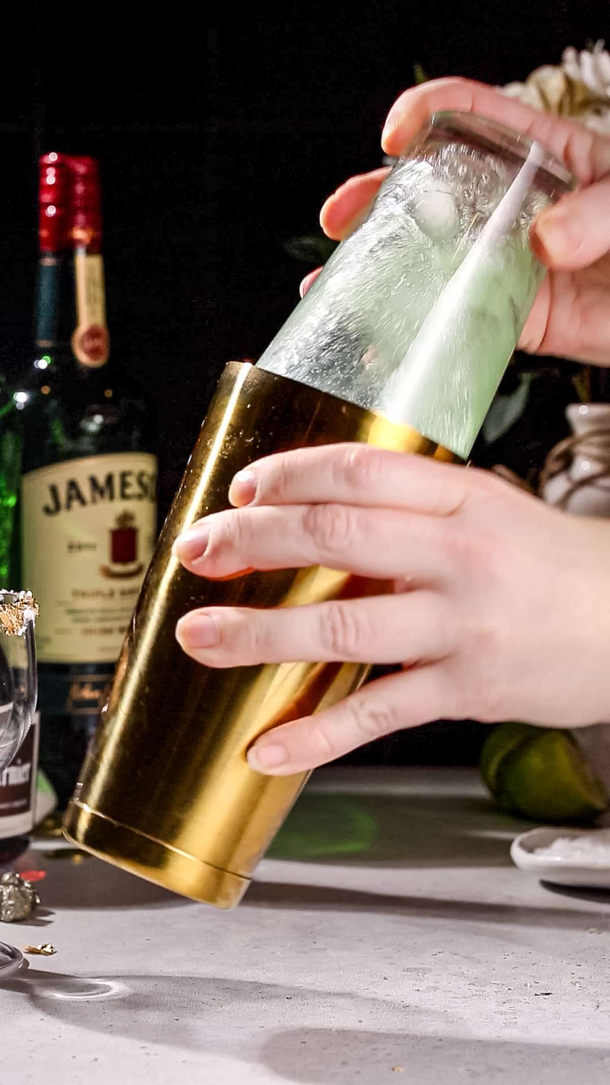 Hands shaking up a green colored cocktail in a cocktail shaker.