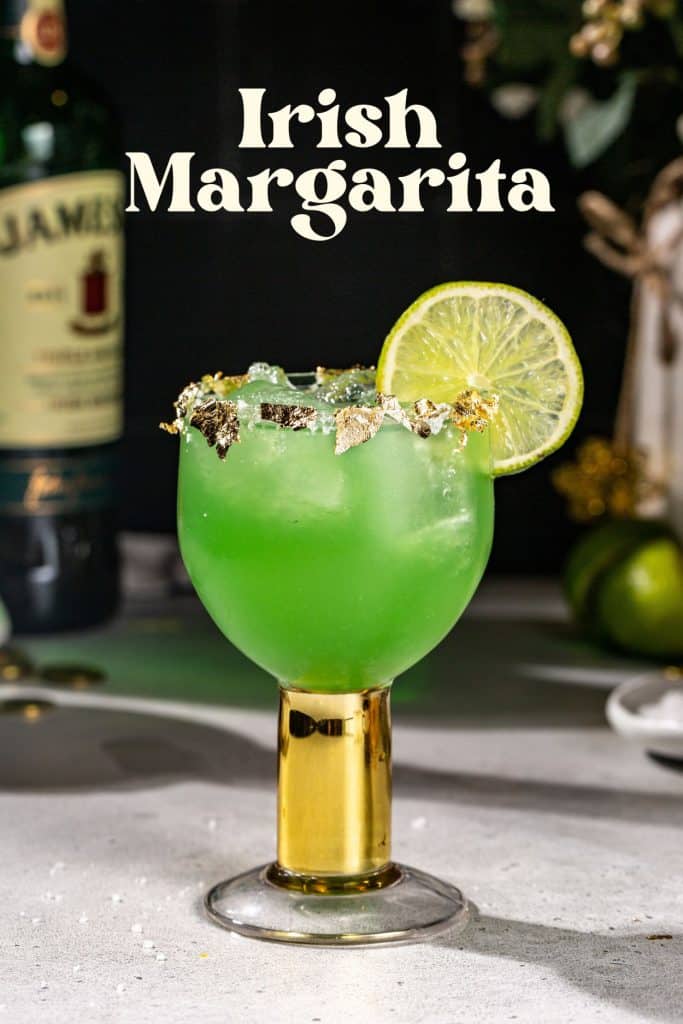 Side view of an Irish Margarita cocktail. The drink is green and has a lime slice as a garnish, along with a salt rim that is decorated with edible gold leaf. Text above the drink says “Irish margarita”.