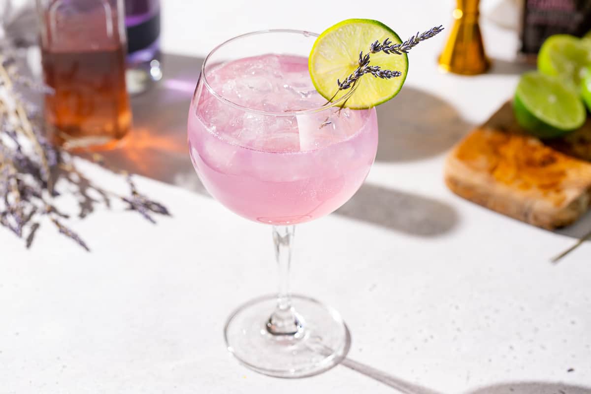 Slightly overhead photo of a Lavender Lime gin spritz cocktail. The drink is a pinkish purple color and garnished with a lime slice and lavender sprigs.