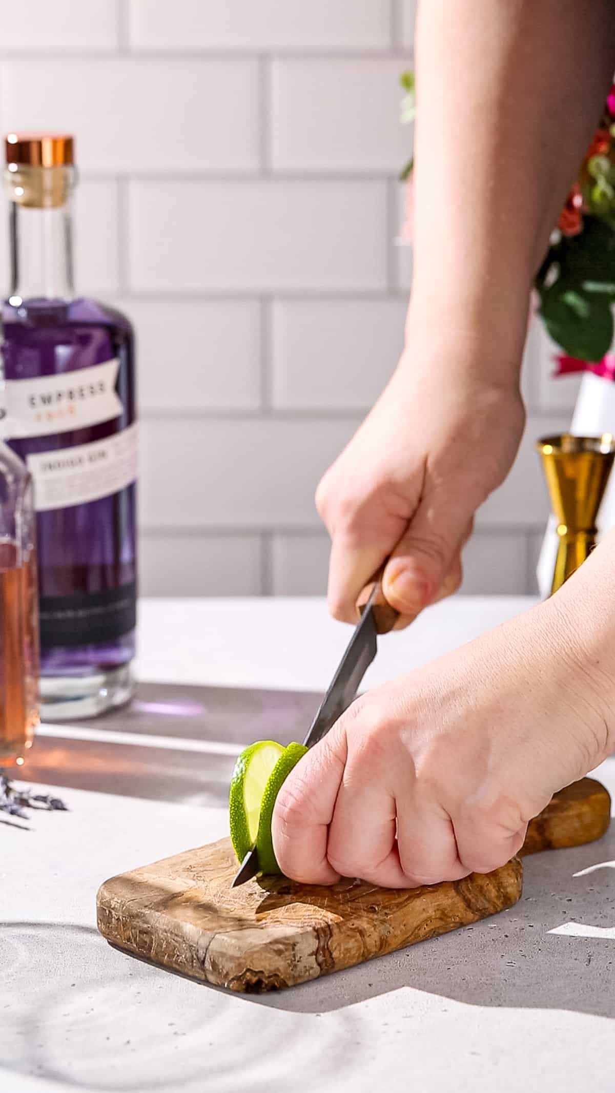 Hands cutting a slice of lime with a knife.