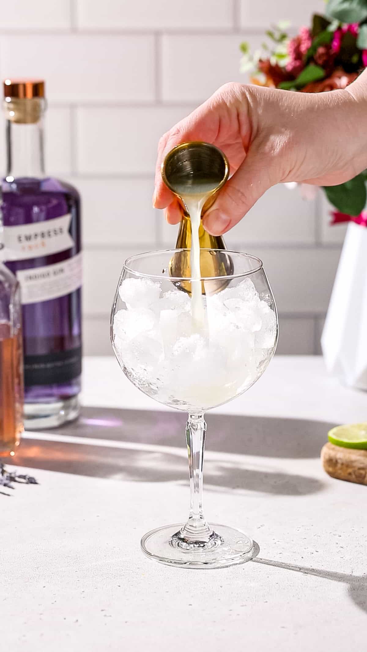 Hand adding lime juice to a cocktail glass using a jigger.