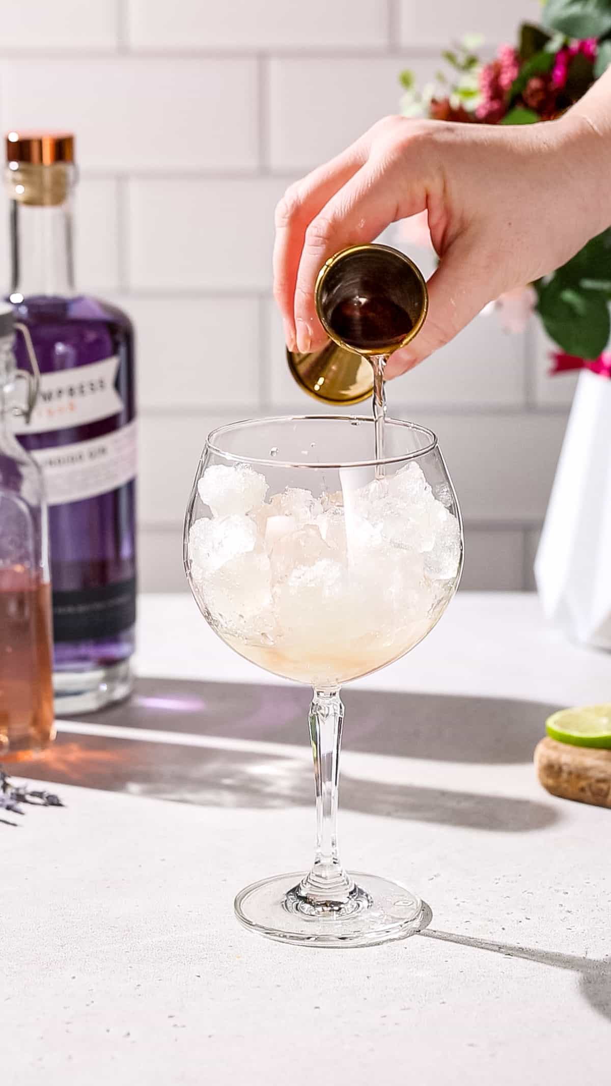 Hand adding lavender syrup to a cocktail glass.