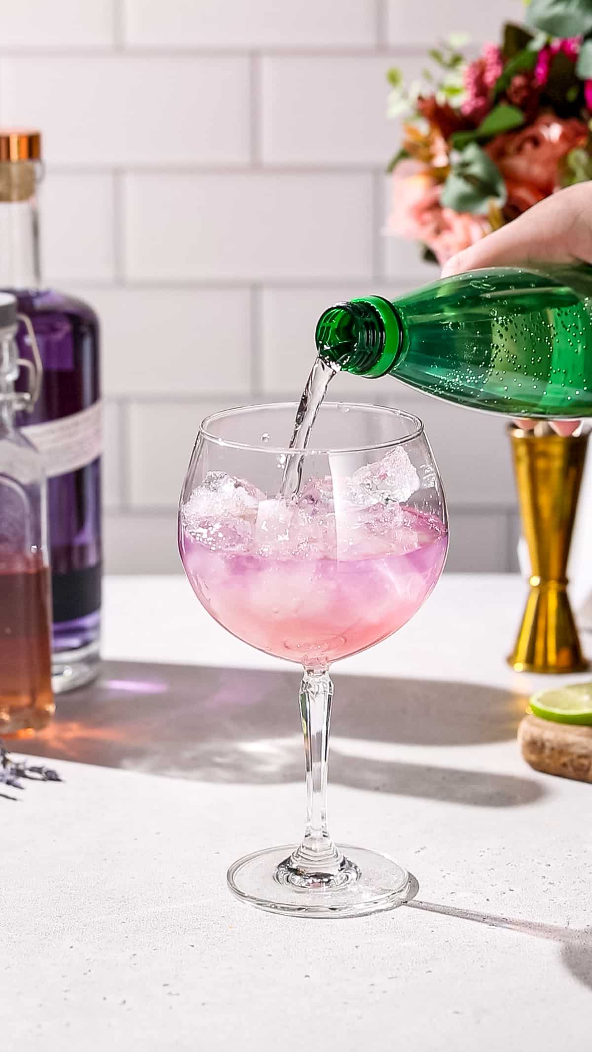 Hand pouring seltzer into a cocktail glass filled with pink liquid.