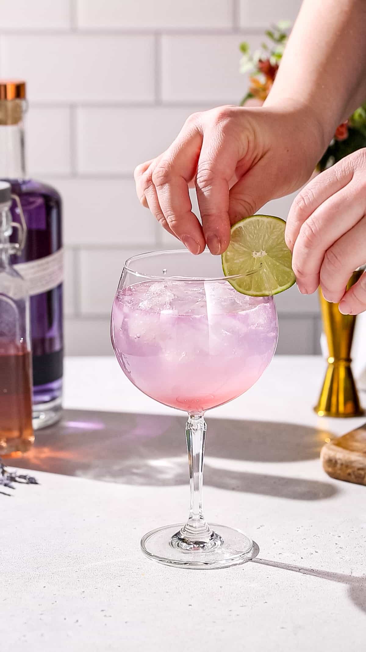 Hand adding a lime slice to a cocktail as a garnish.