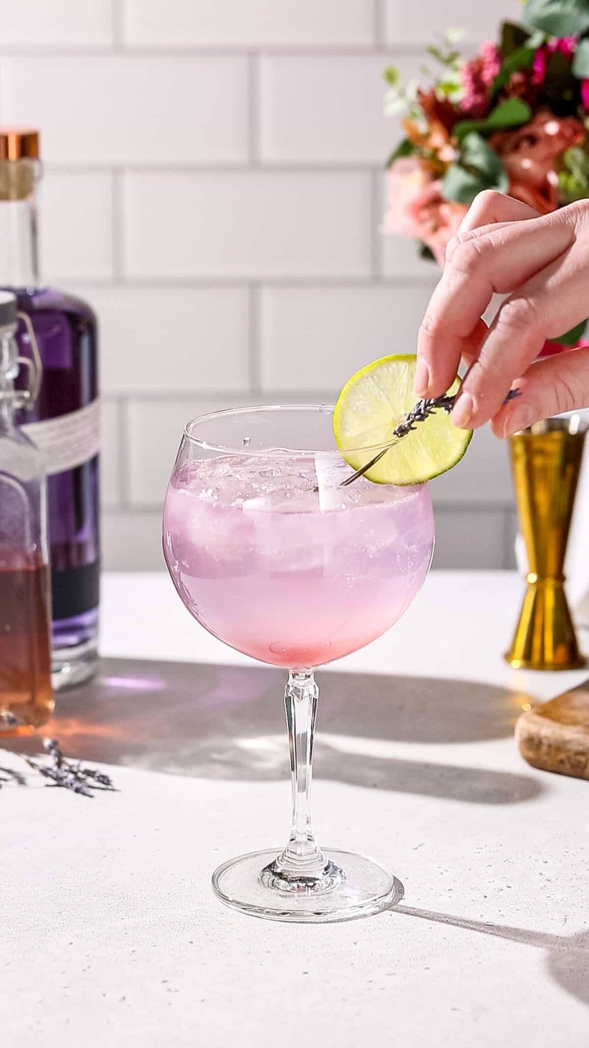 Hand adding lavender sprigs to a pink cocktail as a garnish.