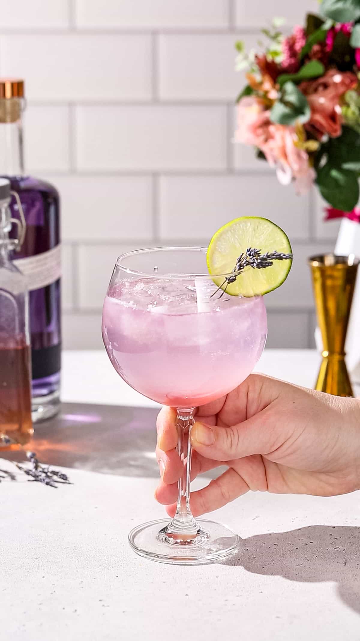 Hand about to pick up a Lavender lime gin spritz cocktail from a countertop.