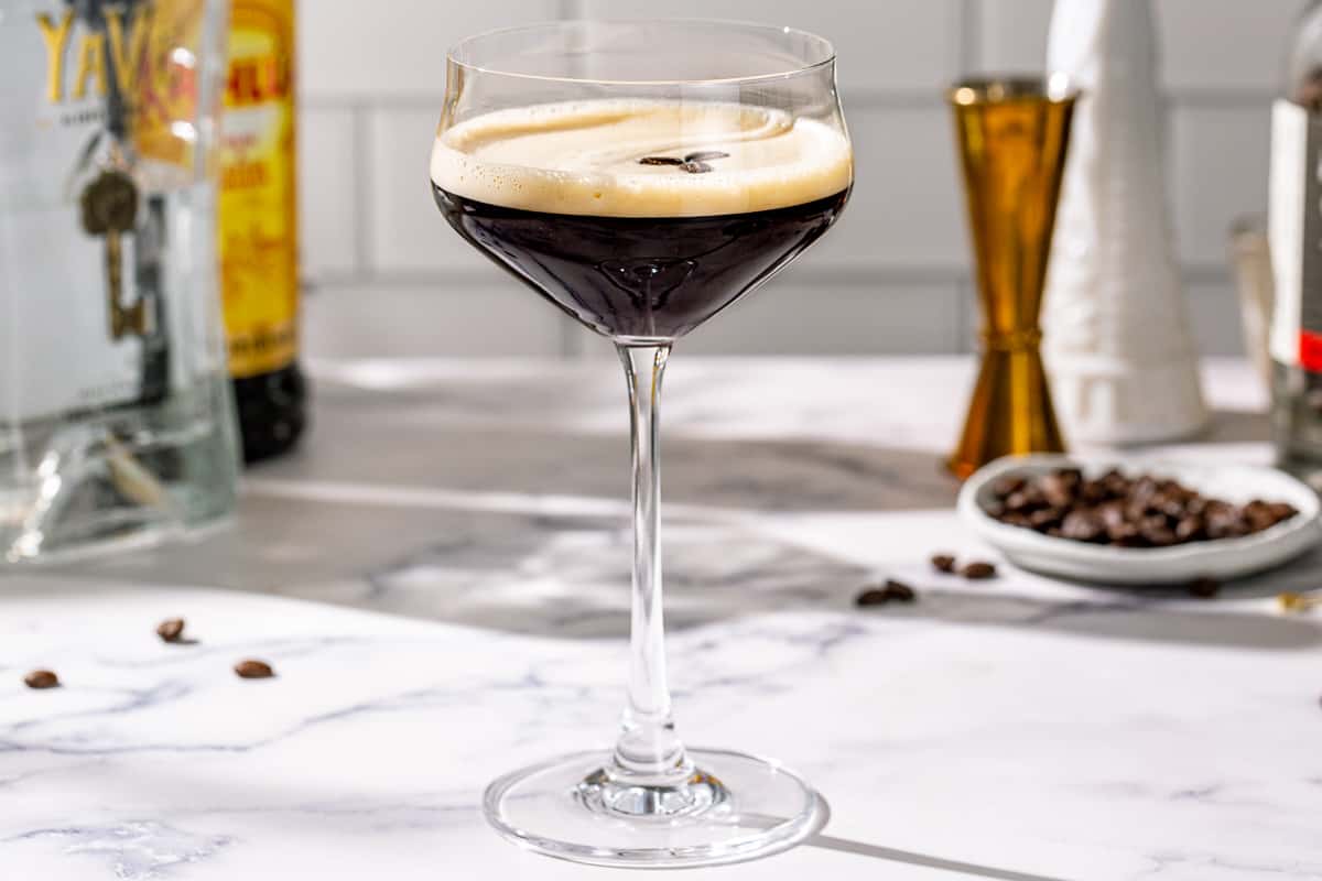 Side view of a Tequila Espresso Martini on a marble countertop. Ingredients and bar tools are in the background.