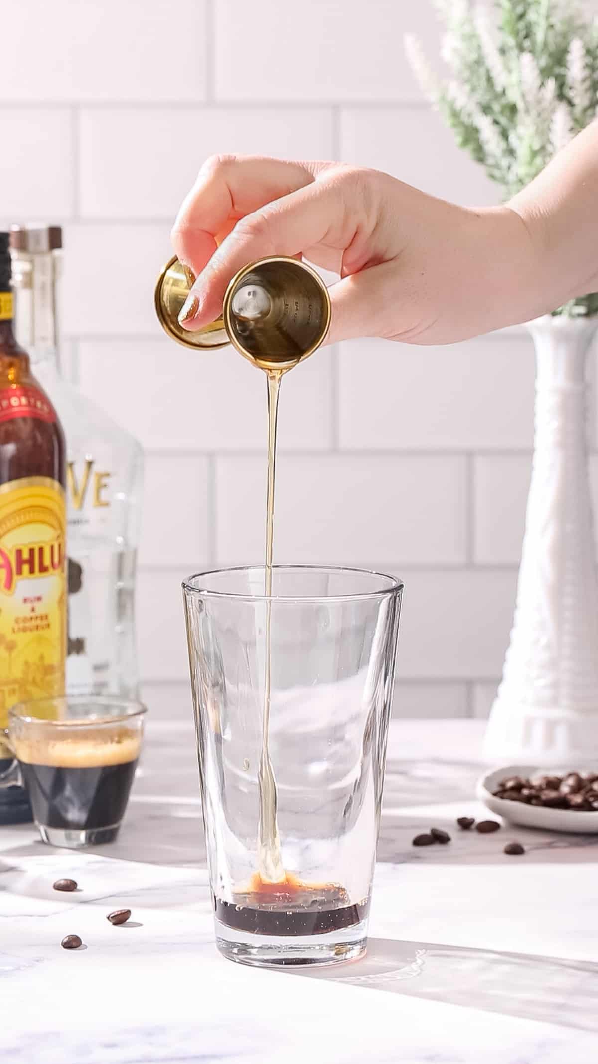 Hand pouring agave nectar from a jigger into a cocktail shaker.