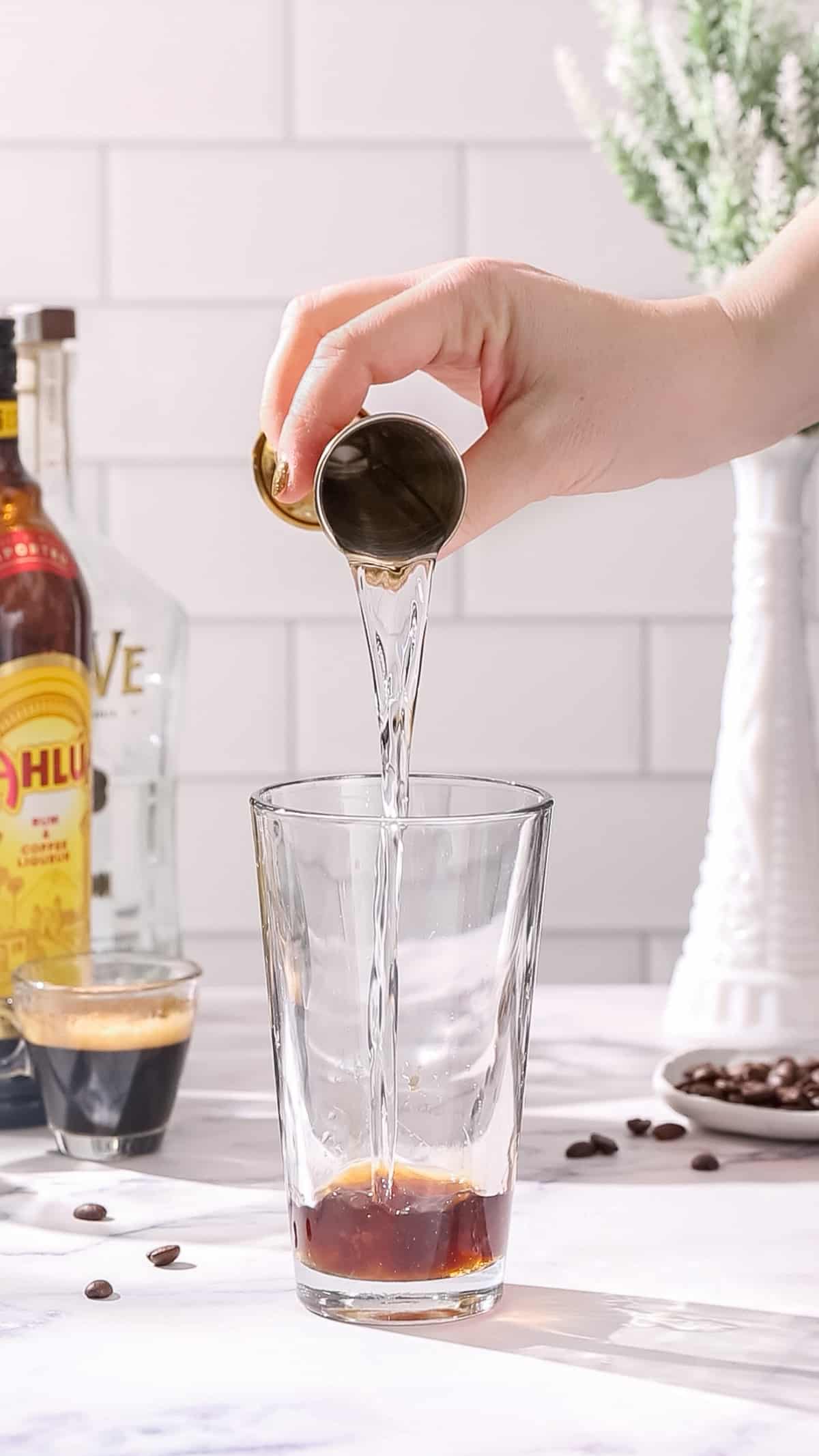 Hand pouring tequila into a cocktail shaker.