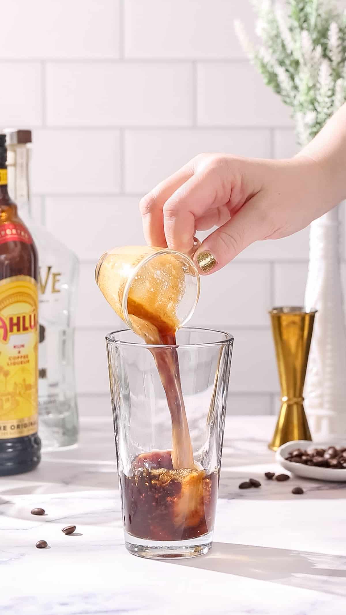 Hand adding a shot of cooled espresso to a cocktail shaker.