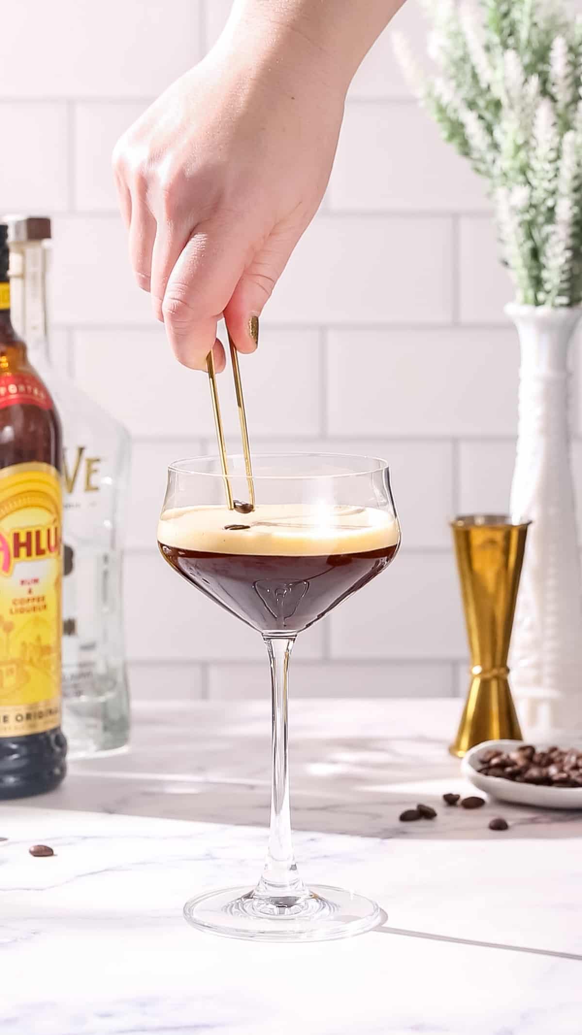 Hand using a pair of culinary tweezers to add coffee beans to the top of a Tequila Espresso Martini.