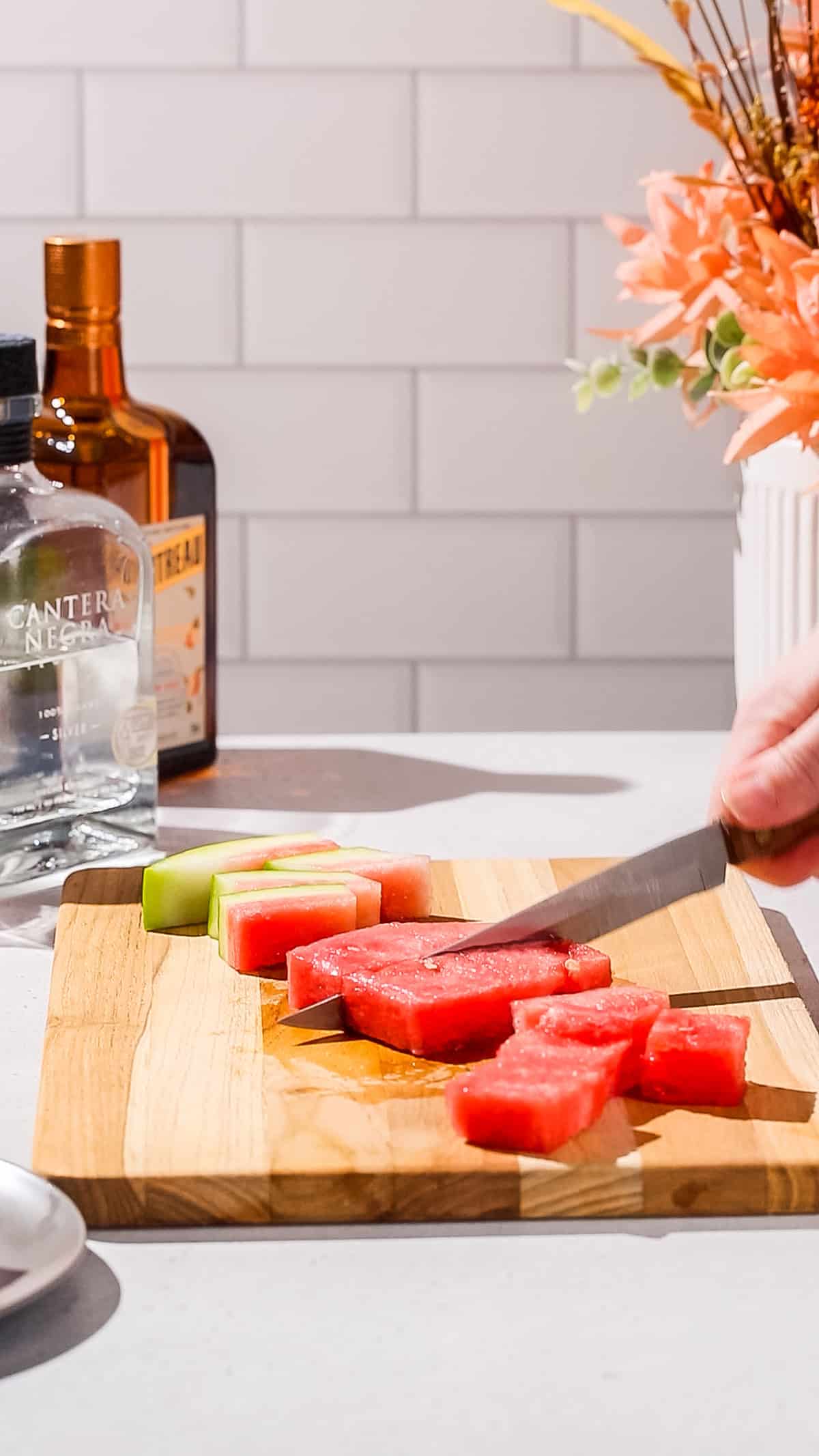 Hand cutting pieces of watermelon with a knife and cutting board.