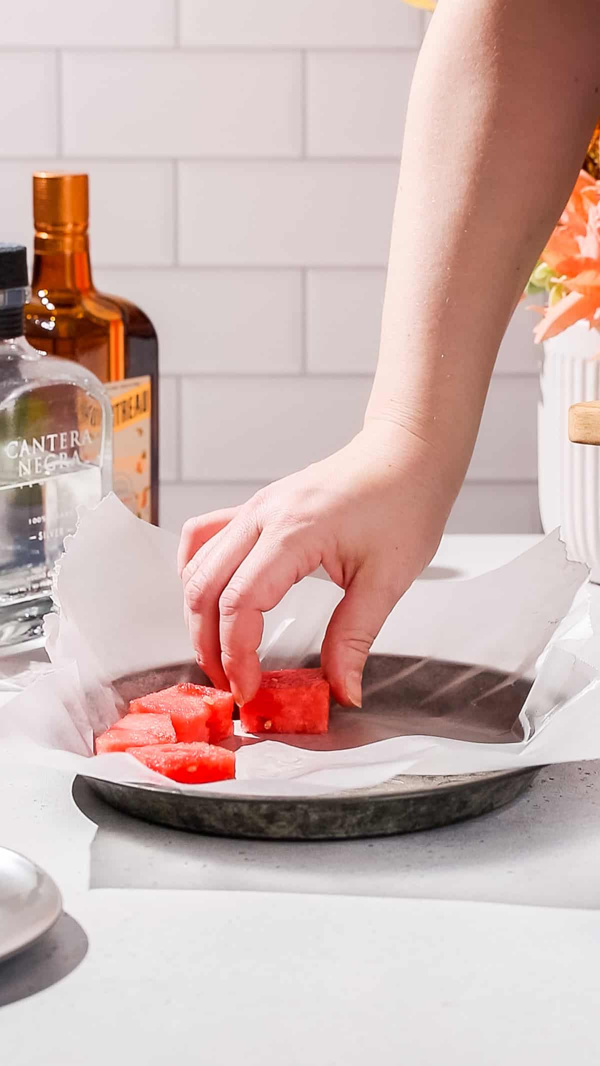 Hand adding watermelon pieces to a baking dish to prepare for freezing them.