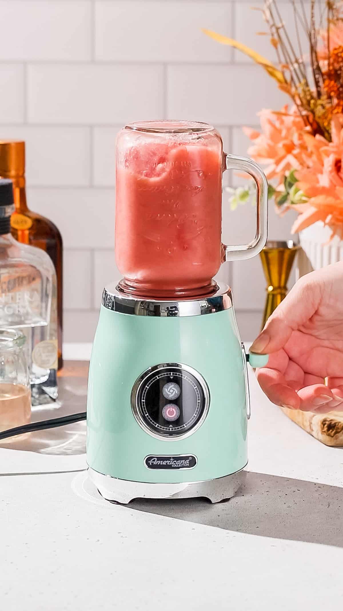 Hand pulsing a personal blender filled with watermelon margarita.